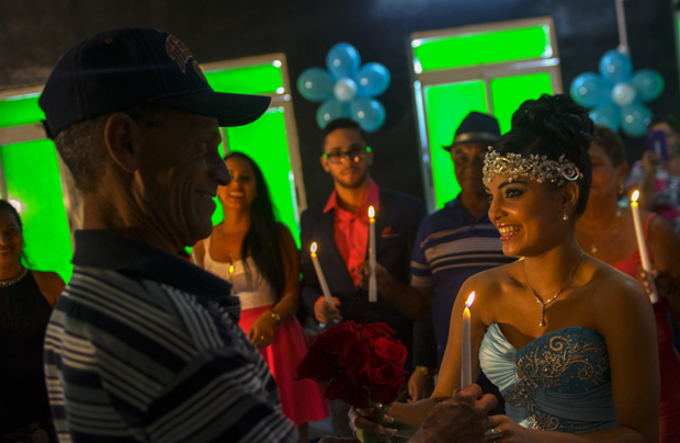 In this Dec. 20, 2015 photo, Daniela Santos Torres, 15, gives a candle to her father as she gifts candles to the most important members of her family during her quinceanera party in the town of Punta Brava near Havana, Cuba. Daniela left Cuba when she was 3, returning in December for her quinceanera photos and party. She now lives in Glendale, Arizona, where her father runs a home remodeling business. She said returning to Cuba for her celebration was a dream, allowing her to include her extended family and friends on the island. (AP Photo/Ramon Espinosa)