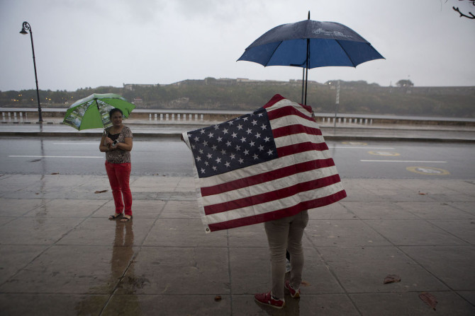 A Cuban man carrying the Stars and Stripes waits in the rain to wave to U.S. President Barack Obama's convoy as it arrives along the Malecon into Old Havana, Cuba, Sunday, March 20, 2016. Obama's trip is a crowning moment in his and Cuban President Raul Castro's ambitious effort to restore normal relations between their countries. (AP Photo/Rebecca Blackwell)